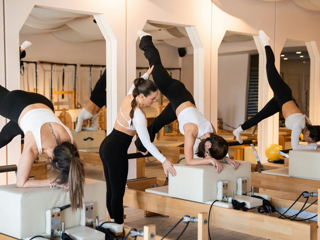 A reformer session, instructor adjusting one client mid movement